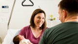An over the shoulder photo of a woman smiling at a man while holding a baby.